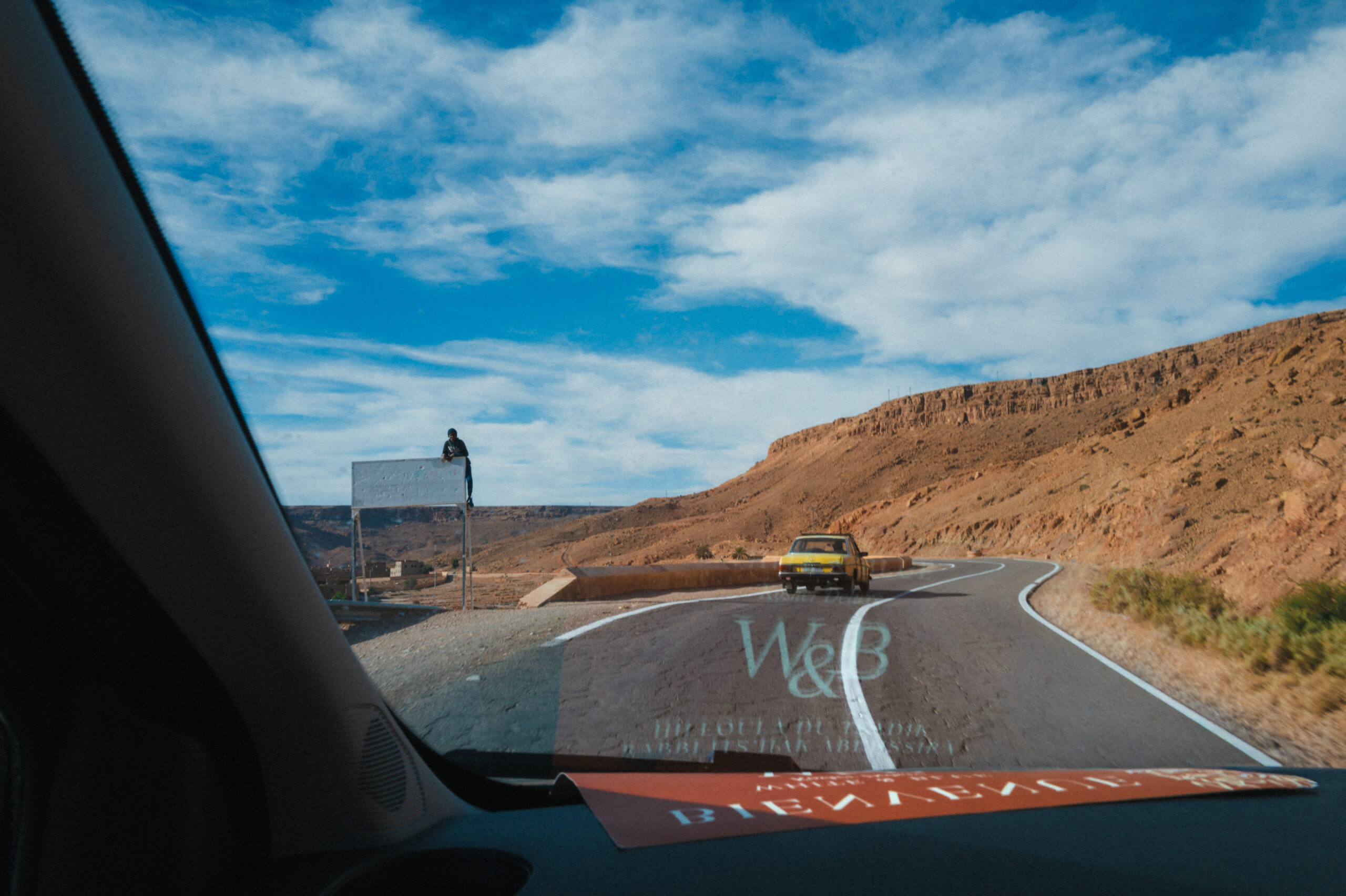 Voiture dans les montagnes marocaine. Un enfant accroché à un panneau d'affichage